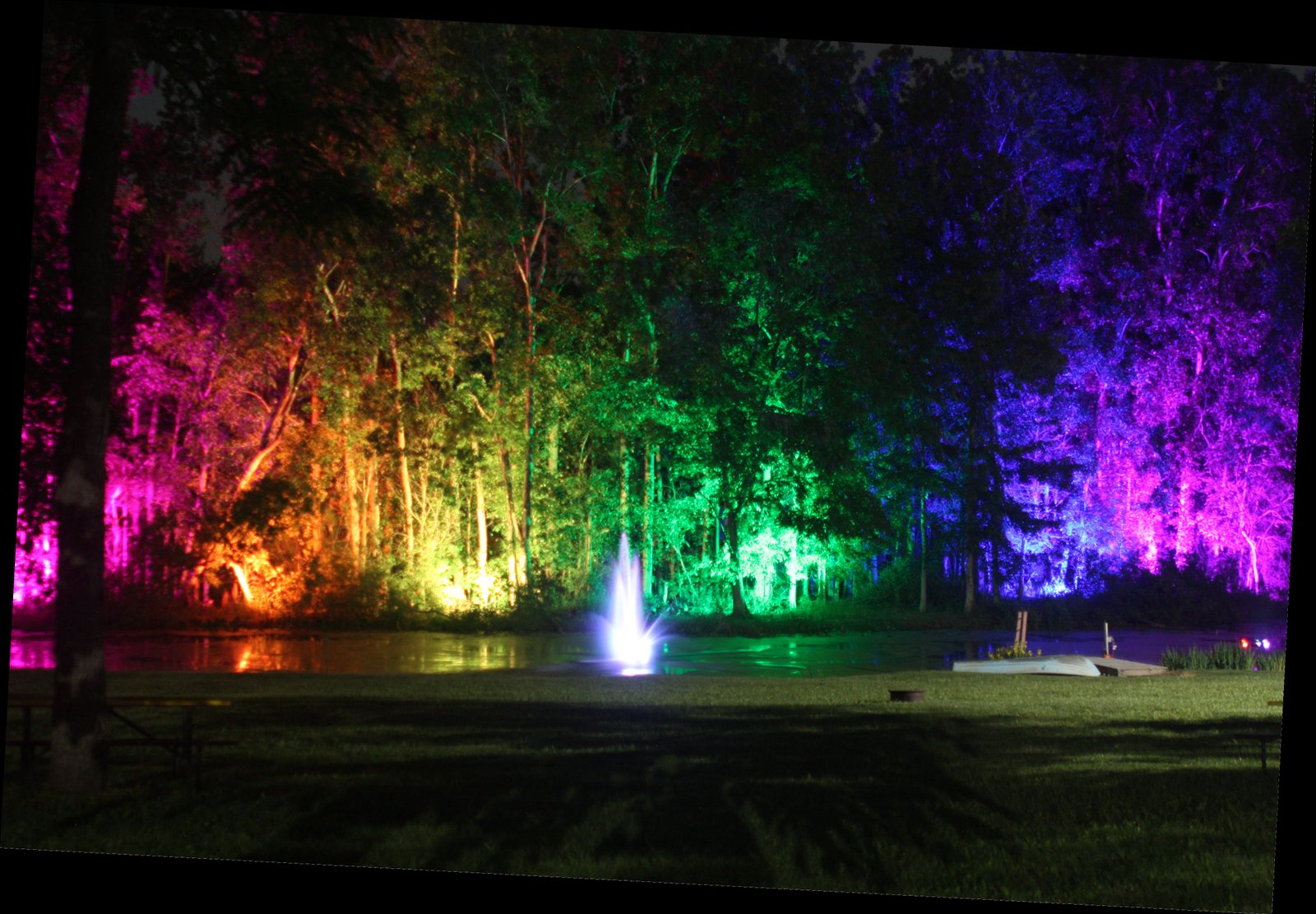 CRC back pond at night with rainbow colored up-lights along the back trees.